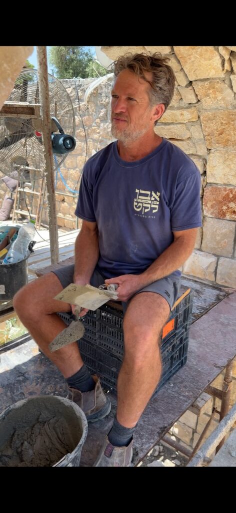 דובי שרר יושב באתר עבודה עם כף טייחים, לובש חולצת אבן לקט