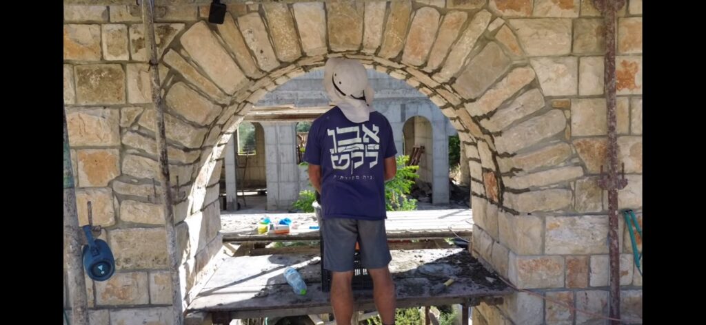 דובי שרר עומד תחת קשת אבן בפרויקט אבן לקט
