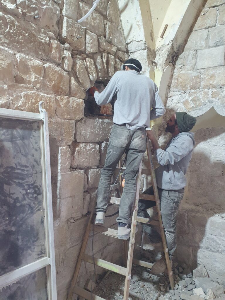 שני פועלים מבצעים כיחול בקיר אבן במסדרון מקומר