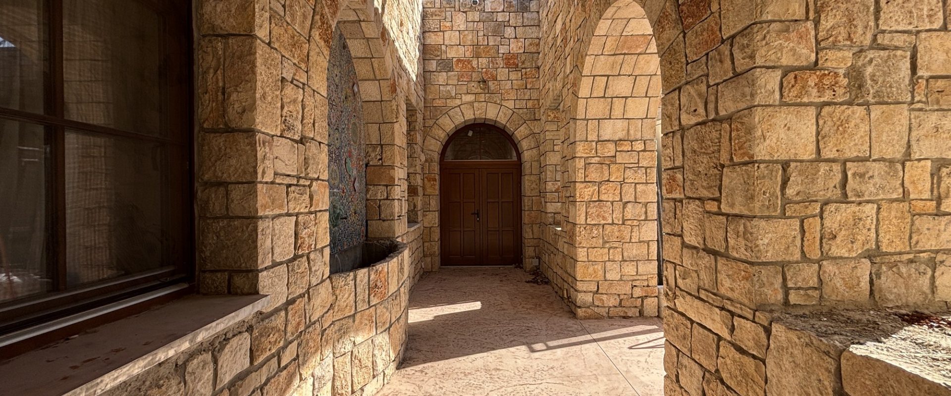 חצר פנימית עם קשתות אבן, דלת עץ מקושתת ומזרקת פסיפס — בית האבן במשמר איילון