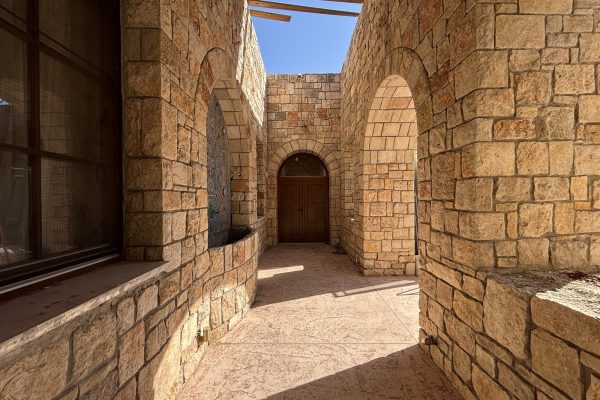 חצר פנימית עם קשתות אבן, דלת עץ מקושתת ומזרקת פסיפס – בית האבן במשמר איילון