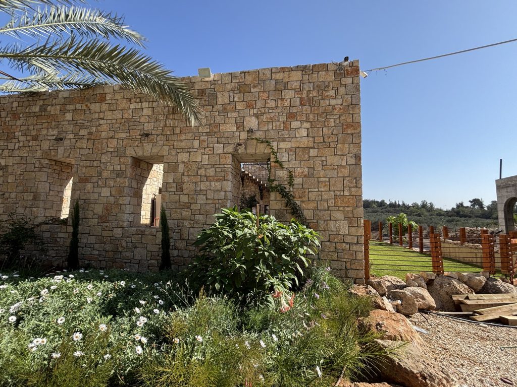 פינת מבנה האבן עם דשא, גדר עץ ונוף פתוח — בית האבן במשמר איילון