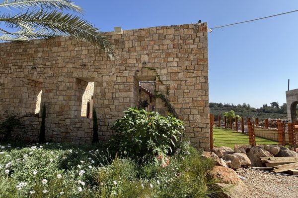 פינת מבנה האבן עם דשא, גדר עץ ונוף פתוח – בית האבן במשמר איילון