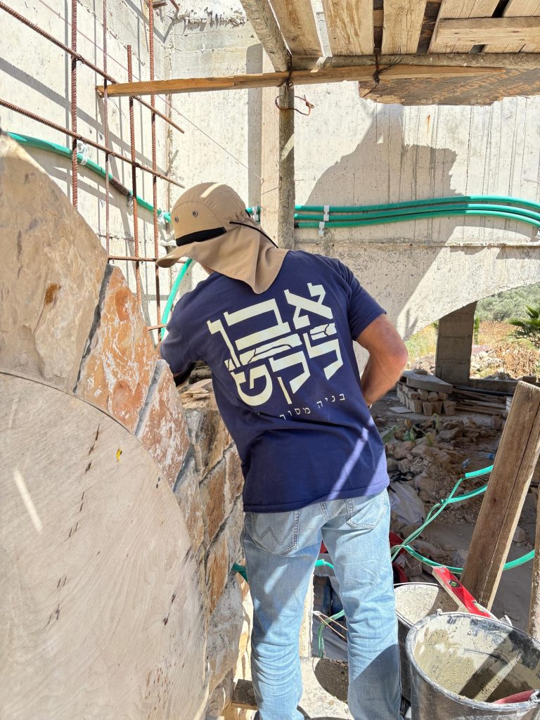 פועל מניח חיפוי אבן על קיר — בית האבן במשמר איילון